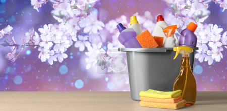 Spring cleaning. Bucket with detergents and tools on wooden surface against blossoming tree, space for text. Banner design-stock-photo