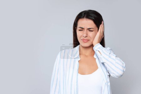Young woman suffering from ear pain on light grey background, space for text
