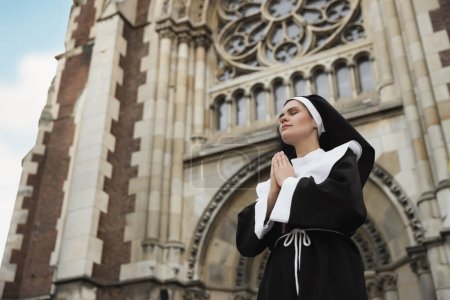 Téléchargez les photos : Young nun with hands clasped together while praying near cathedral outdoors, low angle view. Space for text - en image libre de droit