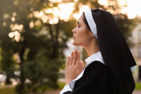 Téléchargez les photos : Young nun with hands clasped together praying outdoors on sunny day, space for text - en image libre de droit