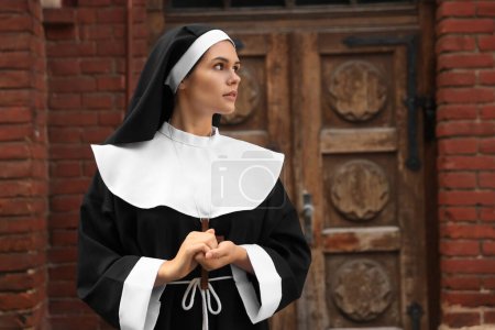 Téléchargez les photos : Jeune religieuse avec croix chrétienne près de vieux bâtiments à l'extérieur - en image libre de droit