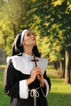 Téléchargez les photos : Jeune religieuse avec croix chrétienne dans le parc par une journée ensoleillée - en image libre de droit