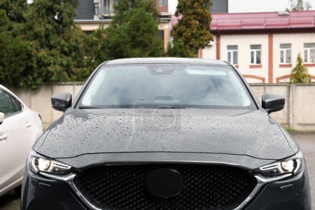 Téléchargez les photos : Black car with switched on headlights in drops of water parked outdoors - en image libre de droit