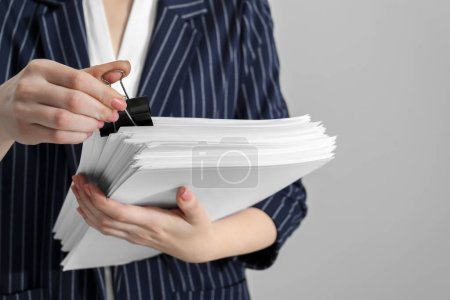 Foto de Woman attaching documents with metal binder clip on grey background, closeup - Imagen libre de derechos