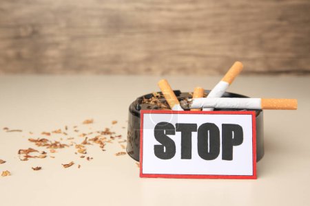 Photo for Card with word Stop, ashtray and cigarette stubs on beige background, space for text. Quitting smoking concept - Royalty Free Image