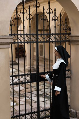 Téléchargez les photos : Young nun in cassock near metal door outdoors - en image libre de droit