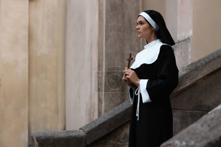 Téléchargez les photos : Jeune religieuse avec croix chrétienne près du bâtiment à l'extérieur - en image libre de droit