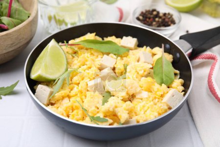 Photo for Frying pan with delicious scrambled eggs, tofu and lime on white table, closeup - Royalty Free Image