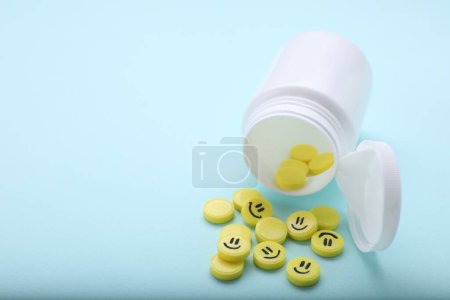 Yellow antidepressants with happy emoticons and medical bottle on light blue background, closeup. Space for text