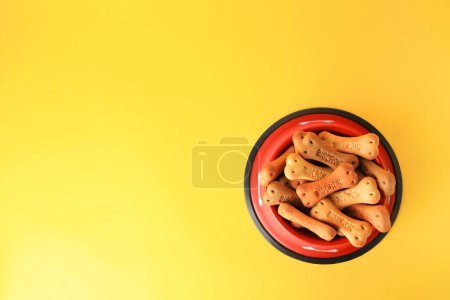 Téléchargez les photos : Biscuits pour chiens en forme d'os dans un bol d'alimentation sur fond jaune, vue de dessus. Espace pour le texte - en image libre de droit