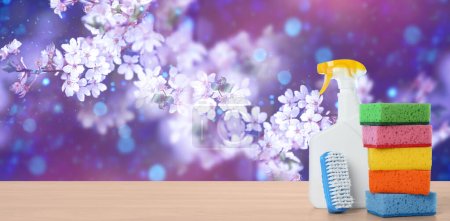 Spring cleaning. Detergents and tools on wooden surface against blossoming tree, space for text. Banner design-stock-photo