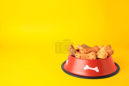 Téléchargez les photos : Biscuits pour chiens en forme d'os dans un bol d'alimentation sur fond jaune, espace pour le texte - en image libre de droit
