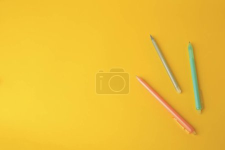 Photo for Three erasable pens on yellow background, flat lay. Space for text - Royalty Free Image