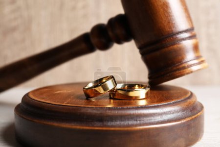 Divorce concept. Wooden gavel and wedding rings on white table, closeup