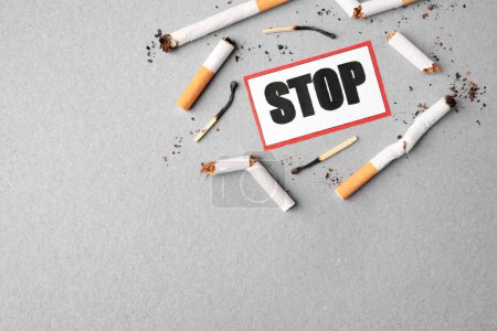 Photo for Quitting smoking concept. Card with word Stop, cigarette waste and burnt matches on light blue background, flat lay. Space for text - Royalty Free Image