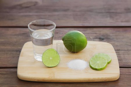 Photo for Mexican tequila shot with lime slices and salt on wooden table. Drink made from agave - Royalty Free Image
