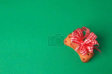 Téléchargez les photos : Bone shaped dog cookie with red bow on green background, top view. Space for text - en image libre de droit