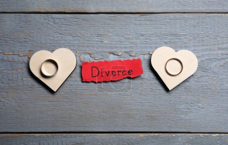 Papierbogen mit Wort Scheidung und Trauringe auf grauem Holztisch, flach gelegt