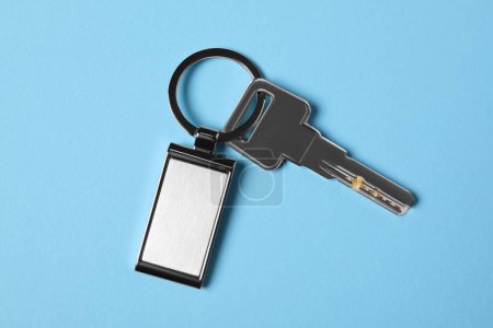 Key with metallic keychain on light blue background, top view