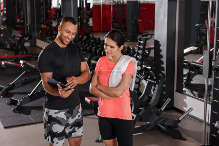Téléchargez les photos : Happy trainer showing young woman workout plan in modern gym, space for text - en image libre de droit