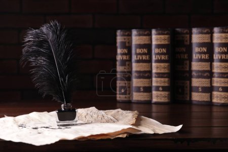 Téléchargez les photos : Encre avec plumes et parchemins vintage près des livres sur table en bois sur fond noir - en image libre de droit