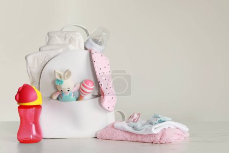 Mother's backpack with baby's stuff on light grey background. Space for text