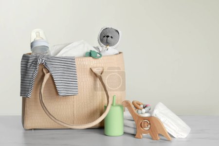 Mother's bag with baby's stuff on light grey background