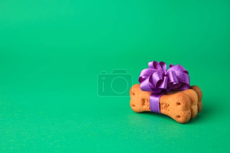 Téléchargez les photos : Cookies pour chien en forme d'os avec noeud violet sur fond vert. Espace pour le texte - en image libre de droit