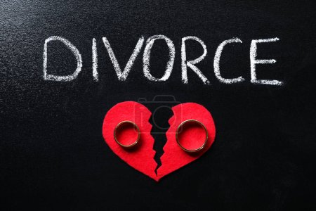 Divorcio de palabras, corazón roto de papel rojo y anillos de boda en pizarra, vista superior