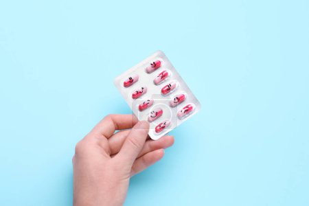 Photo for Woman holding antidepressants with different emoticons on light blue background, top view - Royalty Free Image