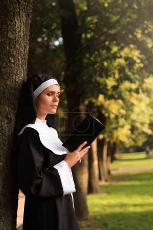 Téléchargez les photos : Young nun reading Bible in park on sunny day - en image libre de droit