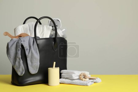 Mother's bag with baby's stuff on yellow surface against grey background. Space for text