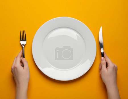 Foto de Woman with empty plate and cutlery on orange background, top view - Imagen libre de derechos