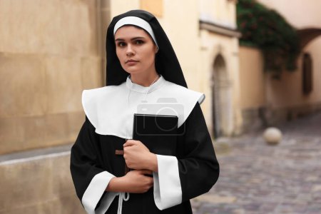 Téléchargez les photos : Young nun with Christian cross and Bible near building outdoors - en image libre de droit