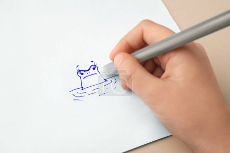 Photo for Child erasing drawing with erasable pen on paper sheet against beige background, closeup - Royalty Free Image
