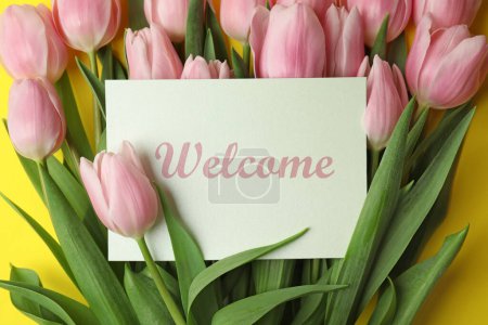Téléchargez les photos : Welcome card among beautiful pink tulips on yellow background, top view - en image libre de droit