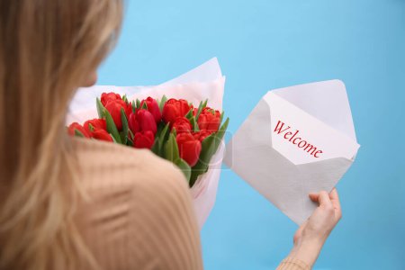 Téléchargez les photos : Welcome card. Woman holding envelope and bouquet of red tulips on light blue background, closeup - en image libre de droit