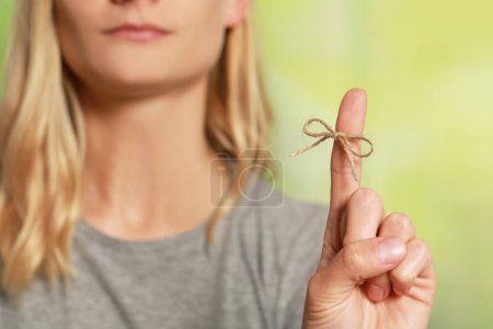 Photo for Woman showing index finger with tied bow as reminder against green blurred background, focus on hand - Royalty Free Image