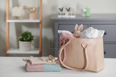 Mother's bag with baby's stuff on white wooden table indoors