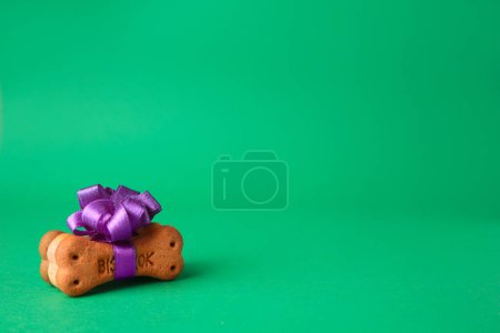 Téléchargez les photos : Bone shaped dog cookies with purple bow on green background. Space for text - en image libre de droit