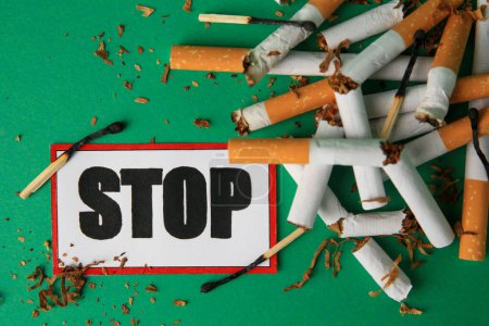 Photo for Stop smoking concept. Card with word Stop, cigarette stubs, tobacco and burnt matches on green background, flat lay - Royalty Free Image