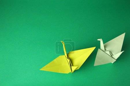Foto de Colorful paper origami cranes on green background, flat lay. Space for text - Imagen libre de derechos