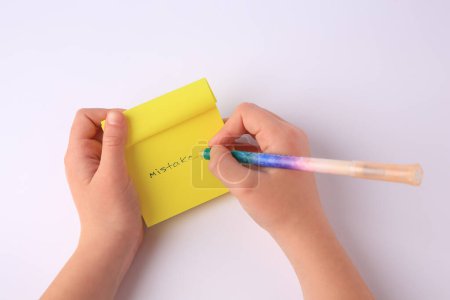 Photo for Child erasing word Mistake written with erasable pen on sticky note against white background, top view - Royalty Free Image
