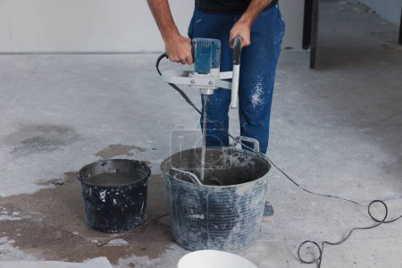 Professional worker mixing cement in bucket indoors, closeup. Tiles installation process