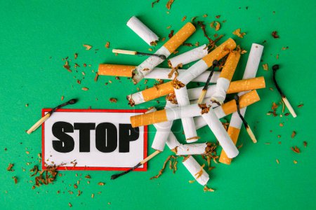 Photo for Stop smoking concept. Card with word Stop, cigarette stubs, tobacco and burnt matches on green background, flat lay - Royalty Free Image