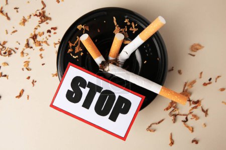 Photo for Card with word Stop, ashtray and cigarette stubs on beige background, flat lay. Quitting smoking concept - Royalty Free Image