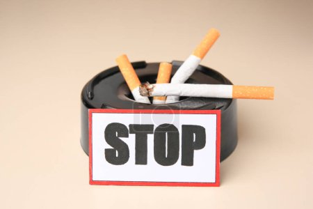 Photo for Card with word Stop, ashtray and cigarette stubs on beige background, closeup. Quitting smoking concept - Royalty Free Image