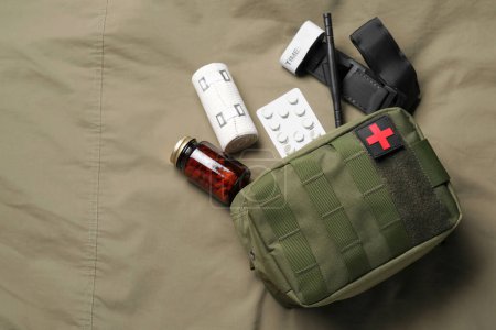 Military first aid kit, tourniquet, pills and elastic bandage on khaki fabric, flat lay. Space for text