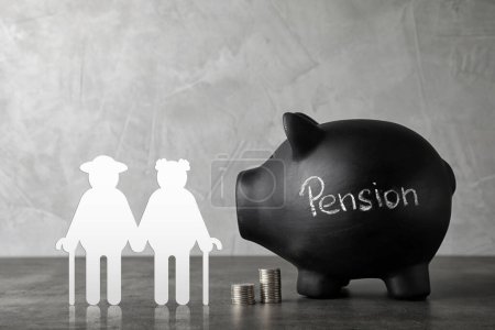 Foto de Pension concept. Elderly couple illustration, coins and piggybank on grey table - Imagen libre de derechos