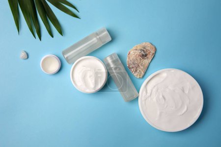 Foto de Flat lay composition with different cosmetic products and palm leaves on light blue background - Imagen libre de derechos